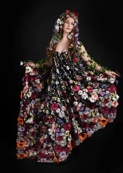 Kelt Bahar Tanrıçası Olarak Kadın Modeli 'nin Portresi Beltane Pagan Mitolojisinden esinlenerek Çiçek Fantezi Pelerini Kostümü. Uzaklaşmak, geriye doğru poz vermek, Karanlık Stüdyo Arkaplanı 'nda soyutlanmak
