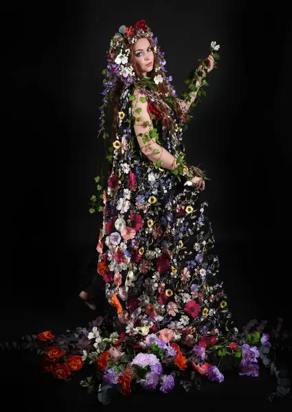 Kelt Bahar Tanrıçası Olarak Kadın Modeli 'nin Portresi Beltane Pagan Mitolojisinden esinlenerek Çiçek Fantezi Pelerini Kostümü. Uzaklaşmak, geriye doğru poz vermek, Karanlık Stüdyo Arkaplanı 'nda soyutlanmak