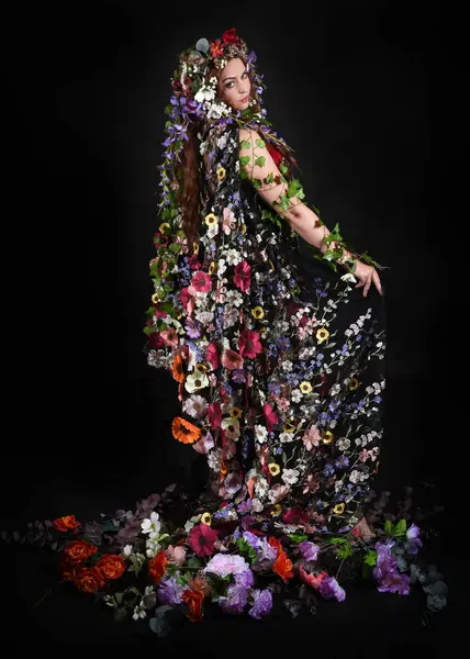 Kelt Bahar Tanrıçası Olarak Kadın Modeli 'nin Portresi Beltane Pagan Mitolojisinden esinlenerek Çiçek Fantezi Pelerini Kostümü. Uzaklaşmak, geriye doğru poz vermek, Karanlık Stüdyo Arkaplanı 'nda soyutlanmak