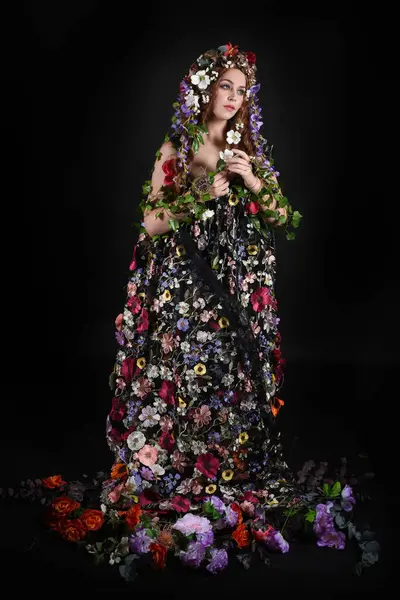 Kelt Bahar Tanrıçası Olarak Kadın Modeli 'nin Portresi Beltane Pagan Mitolojisinden esinlenerek Çiçek Fantezi Pelerini Kostümü. Uzaklaşmak, geriye doğru poz vermek, Karanlık Stüdyo Arkaplanı 'nda soyutlanmak