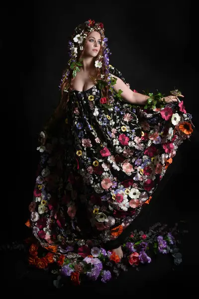 Kelt Bahar Tanrıçası Olarak Kadın Modeli 'nin Portresi Beltane Pagan Mitolojisinden esinlenerek Çiçek Fantezi Pelerini Kostümü. Uzaklaşmak, geriye doğru poz vermek, Karanlık Stüdyo Arkaplanı 'nda soyutlanmak
