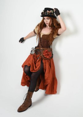 Uzun, yürüyen Steampunk Botanikçisi, çılgın bilim adamı, silindir şapkalı ve gözlüklü kadın model. Kızıl Saçlı Fantezi Karakteri Beyaz Stüdyo Arkaplanında Pozisyon