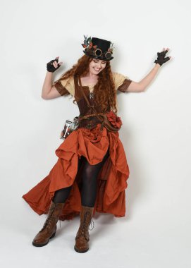 Uzun, yürüyen Steampunk Botanikçisi, çılgın bilim adamı, silindir şapkalı ve gözlüklü kadın model. Kızıl Saçlı Fantezi Karakteri Beyaz Stüdyo Arkaplanında Pozisyon