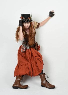 Uzun, yürüyen Steampunk Botanikçisi, çılgın bilim adamı, silindir şapkalı ve gözlüklü kadın model. Kızıl Saçlı Fantezi Karakteri Beyaz Stüdyo Arkaplanında Pozisyon