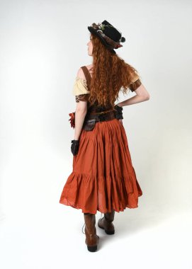 Uzun, yürüyen Steampunk Botanikçisi, çılgın bilim adamı, silindir şapkalı ve gözlüklü kadın model. Kızıl Saçlı Fantezi Karakteri Beyaz Stüdyo Arkaplanında Pozisyon