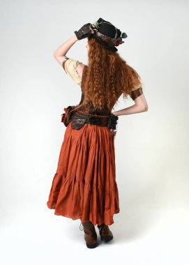 Uzun, yürüyen Steampunk Botanikçisi, çılgın bilim adamı, silindir şapkalı ve gözlüklü kadın model. Kızıl Saçlı Fantezi Karakteri Beyaz Stüdyo Arkaplanında Pozisyon