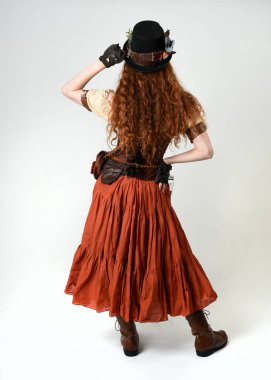 Uzun, yürüyen Steampunk Botanikçisi, çılgın bilim adamı, silindir şapkalı ve gözlüklü kadın model. Kızıl Saçlı Fantezi Karakteri Beyaz Stüdyo Arkaplanında Pozisyon