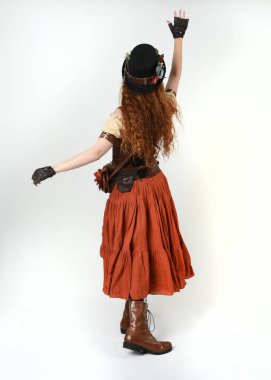 Uzun, yürüyen Steampunk Botanikçisi, çılgın bilim adamı, silindir şapkalı ve gözlüklü kadın model. Kızıl Saçlı Fantezi Karakteri Beyaz Stüdyo Arkaplanında Pozisyon
