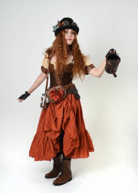 Uzun, yürüyen Steampunk Botanikçisi, çılgın bilim adamı, silindir şapkalı ve gözlüklü kadın model. Kızıl Saçlı Fantezi Karakteri. Elinde su dolu bir kutu var. İzole edilmiş Beyaz Stüdyo Arkaplanı 'nda silah gibi.