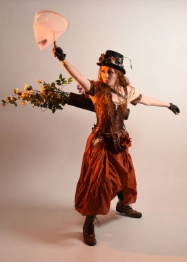 Uzun, yürüyen Steampunk Botanikçisi, çılgın bilim adamı, silindir şapkalı ve gözlüklü kadın model. Kızıl Saçlı Fantezi Karakteri Poz Kelebek Avlama Ağı, Stüdyo Arkaplan