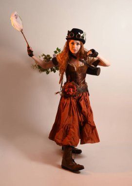 Uzun, yürüyen Steampunk Botanikçisi, çılgın bilim adamı, silindir şapkalı ve gözlüklü kadın model. Kızıl Saçlı Fantezi Karakteri Poz Kelebek Avlama Ağı, Stüdyo Arkaplan