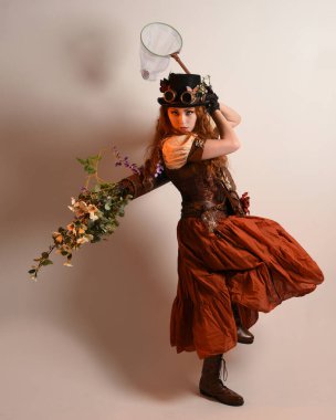 Uzun, yürüyen Steampunk Botanikçisi, çılgın bilim adamı, silindir şapkalı ve gözlüklü kadın model. Kızıl Saçlı Fantezi Karakteri Poz Kelebek Avlama Ağı, Stüdyo Arkaplan