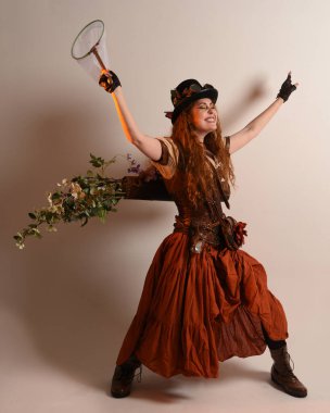Uzun, yürüyen Steampunk Botanikçisi, çılgın bilim adamı, silindir şapkalı ve gözlüklü kadın model. Kızıl Saçlı Fantezi Karakteri Poz Kelebek Avlama Ağı, Stüdyo Arkaplan