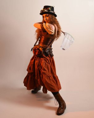 Uzun, yürüyen Steampunk Botanikçisi, çılgın bilim adamı, silindir şapkalı ve gözlüklü kadın model. Kızıl Saçlı Fantezi Karakteri Poz Kelebek Avlama Ağı, Stüdyo Arkaplan