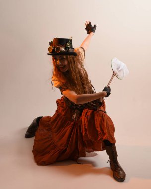 Uzun, yürüyen Steampunk Botanikçisi, çılgın bilim adamı, silindir şapkalı ve gözlüklü kadın model. Kızıl Saçlı Fantezi Karakteri Poz Kelebek Avlama Ağı, Stüdyo Arkaplan