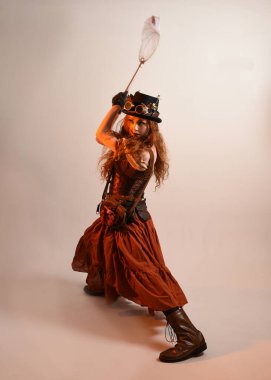 Uzun, yürüyen Steampunk Botanikçisi, çılgın bilim adamı, silindir şapkalı ve gözlüklü kadın model. Kızıl Saçlı Fantezi Karakteri Poz Kelebek Avlama Ağı, Stüdyo Arkaplan