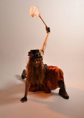 Uzun, yürüyen Steampunk Botanikçisi, çılgın bilim adamı, silindir şapkalı ve gözlüklü kadın model. Kızıl Saçlı Fantezi Karakteri Poz Kelebek Avlama Ağı, Stüdyo Arkaplan
