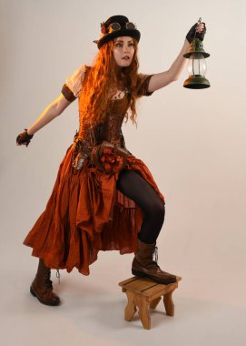 Uzun, yürüyen Steampunk Botanikçisi, çılgın bilim adamı, silindir şapkalı ve gözlüklü kadın model. Kızıl Saçlı Fantezi Karakteri Poz Fenerinde Fener Stüdyo Arkaplanı