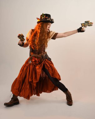 Uzun, yürüyen Steampunk Botanikçisi, çılgın bilim adamı, silindir şapkalı ve gözlüklü kadın model. Kızıl Saçlı Fantezi Karakteri. Elinde silah olan bir poz, stüdyo arka planı.