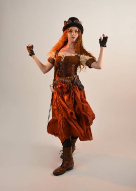 Uzun, yürüyen Steampunk Botanikçisi, çılgın bilim adamı, silindir şapkalı ve gözlüklü kadın model. Kızıl Saçlı Fantezi Karakteri Beyaz Stüdyo Arkaplanında Pozisyon