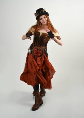 Uzun, yürüyen Steampunk Botanikçisi, çılgın bilim adamı, silindir şapkalı ve gözlüklü kadın model. Kızıl Saçlı Fantezi Karakteri Beyaz Stüdyo Arkaplanında Pozisyon