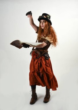Uzun, yürüyen Steampunk Botanikçisi, çılgın bilim adamı, silindir şapkalı ve gözlüklü kadın model. Kızıl Saçlı Fantezi Karakteri Poz Beyaz Stüdyo Arkaplanı hakkında akademik kitaplar tutuyor
