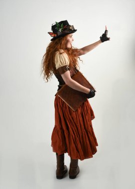 Uzun, yürüyen Steampunk Botanikçisi, çılgın bilim adamı, silindir şapkalı ve gözlüklü kadın model. Kızıl Saçlı Fantezi Karakteri Poz Beyaz Stüdyo Arkaplanı hakkında akademik kitaplar tutuyor