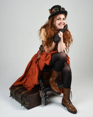 Uzun, yürüyen Steampunk Botanikçisi, çılgın bilim adamı, silindir şapkalı ve gözlüklü kadın model. Kızıl Saçlı Fantezi Karakteri Beyaz Stüdyo Arkaplanı 'nda poz veriyor