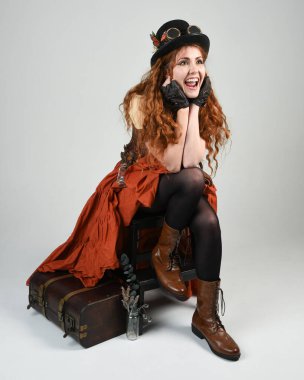 Uzun, yürüyen Steampunk Botanikçisi, çılgın bilim adamı, silindir şapkalı ve gözlüklü kadın model. Kızıl Saçlı Fantezi Karakteri Beyaz Stüdyo Arkaplanı 'nda poz veriyor