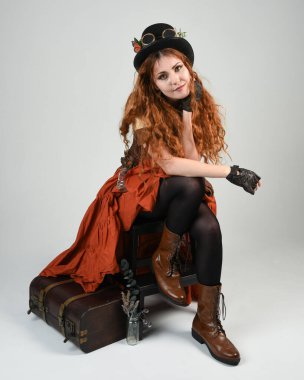 Uzun, yürüyen Steampunk Botanikçisi, çılgın bilim adamı, silindir şapkalı ve gözlüklü kadın model. Kızıl Saçlı Fantezi Karakteri Beyaz Stüdyo Arkaplanı 'nda poz veriyor