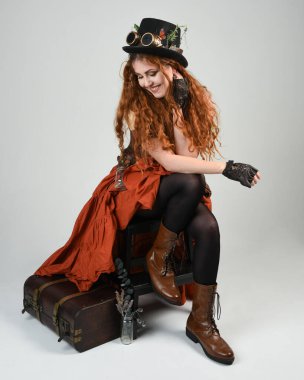 Uzun, yürüyen Steampunk Botanikçisi, çılgın bilim adamı, silindir şapkalı ve gözlüklü kadın model. Kızıl Saçlı Fantezi Karakteri Beyaz Stüdyo Arkaplanı 'nda poz veriyor