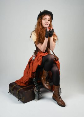 Uzun, yürüyen Steampunk Botanikçisi, çılgın bilim adamı, silindir şapkalı ve gözlüklü kadın model. Kızıl Saçlı Fantezi Karakteri Beyaz Stüdyo Arkaplanı 'nda poz veriyor