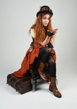 Uzun, yürüyen Steampunk Botanikçisi, çılgın bilim adamı, silindir şapkalı ve gözlüklü kadın model. Kızıl Saçlı Fantezi Karakteri Beyaz Stüdyo Arkaplanı 'nda poz veriyor