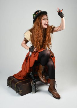 Uzun, yürüyen Steampunk Botanikçisi, çılgın bilim adamı, silindir şapkalı ve gözlüklü kadın model. Kızıl Saçlı Fantezi Karakteri Beyaz Stüdyo Arkaplanı 'nda poz veriyor