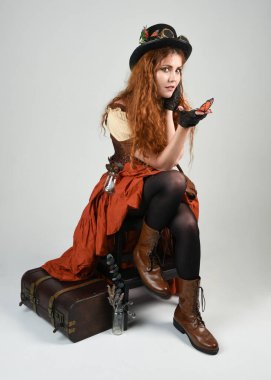 Uzun, yürüyen Steampunk Botanikçisi, çılgın bilim adamı, silindir şapkalı ve gözlüklü kadın model. Kızıl Saçlı Fantezi Karakteri Beyaz Stüdyo Arkaplanı 'nda poz veriyor