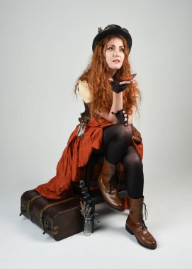 Uzun, yürüyen Steampunk Botanikçisi, çılgın bilim adamı, silindir şapkalı ve gözlüklü kadın model. Kızıl Saçlı Fantezi Karakteri Beyaz Stüdyo Arkaplanı 'nda poz veriyor