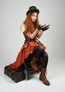 Uzun, yürüyen Steampunk Botanikçisi, çılgın bilim adamı, silindir şapkalı ve gözlüklü kadın model. Kızıl Saçlı Fantezi Karakteri Beyaz Stüdyo Arkaplanı 'nda poz veriyor