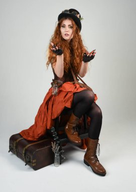 Uzun, yürüyen Steampunk Botanikçisi, çılgın bilim adamı, silindir şapkalı ve gözlüklü kadın model. Kızıl Saçlı Fantezi Karakteri Beyaz Stüdyo Arkaplanı 'nda poz veriyor