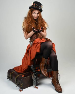 Uzun, yürüyen Steampunk Botanikçisi, çılgın bilim adamı, silindir şapkalı ve gözlüklü kadın model. Kızıl Saçlı Fantezi Karakteri Beyaz Stüdyo Arkaplanı 'nda poz veriyor