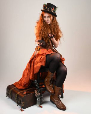 Uzun, yürüyen Steampunk Botanikçisi, çılgın bilim adamı, silindir şapkalı ve gözlüklü kadın model. Kızıl Saçlı Fantezi Karakteri Beyaz Stüdyo Arkaplanı 'nda poz veriyor