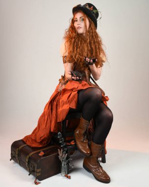 Uzun, yürüyen Steampunk Botanikçisi, çılgın bilim adamı, silindir şapkalı ve gözlüklü kadın model. Kızıl Saçlı Fantezi Karakteri Beyaz Stüdyo Arkaplanı 'nda poz veriyor