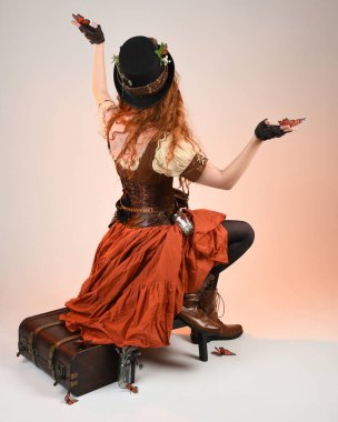 Uzun, yürüyen Steampunk Botanikçisi, çılgın bilim adamı, silindir şapkalı ve gözlüklü kadın model. Kızıl Saçlı Fantezi Karakteri Beyaz Stüdyo Arkaplanı 'nda poz veriyor