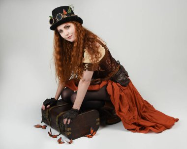 Steampunk Botanikçisi, deli bilim adamı, silindir şapkalı ve gözlüklü kadın model. Kızıl Saçlı Fantezi Karakteri Beyaz Stüdyo Arkaplanda Kelebeklerle Poz Veriyor