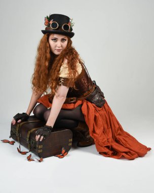 Steampunk Botanikçisi, deli bilim adamı, silindir şapkalı ve gözlüklü kadın model. Kızıl Saçlı Fantezi Karakteri Beyaz Stüdyo Arkaplanda Kelebeklerle Poz Veriyor