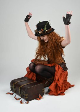 Steampunk Botanikçisi, deli bilim adamı, silindir şapkalı ve gözlüklü kadın model. Kızıl Saçlı Fantezi Karakteri Beyaz Stüdyo Arkaplanda Kelebeklerle Poz Veriyor