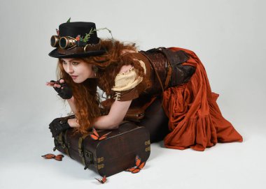 Steampunk Botanikçisi, deli bilim adamı, silindir şapkalı ve gözlüklü kadın model. Kızıl Saçlı Fantezi Karakteri Beyaz Stüdyo Arkaplanda Kelebeklerle Poz Veriyor