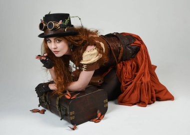 Steampunk Botanikçisi, deli bilim adamı, silindir şapkalı ve gözlüklü kadın model. Kızıl Saçlı Fantezi Karakteri Beyaz Stüdyo Arkaplanda Kelebeklerle Poz Veriyor