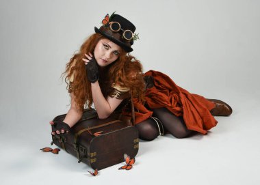 Steampunk Botanikçisi, deli bilim adamı, silindir şapkalı ve gözlüklü kadın model. Kızıl Saçlı Fantezi Karakteri Beyaz Stüdyo Arkaplanda Kelebeklerle Poz Veriyor