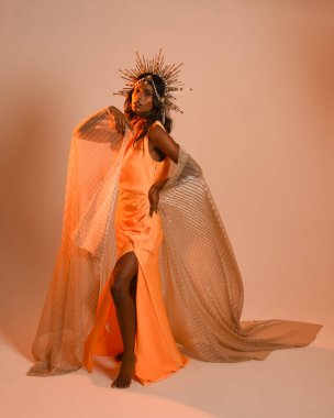 Güzel esmer bir kadının portresi. Fantezi tacını takıyor ve göz alıcı sarı bir balo elbisesi giyiyor. Sinematik renkli ışıklandırmayla stüdyonun arka planında zarif bir poz..