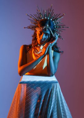 Güzel esmer bir kadının portresi. Fantezi tacını takıyor ve göz alıcı sarı bir balo elbisesi giyiyor. Sinematik renkli ışıklandırmayla stüdyonun arka planında zarif bir poz..